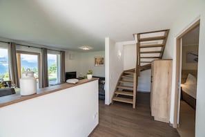 Un interior modern amb una escala de fusta, una cuina i vistes a través de grans finestres.