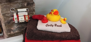 A bathroom with a bathtub, a towel rack with toiletries, and rubber ducks on a towel.