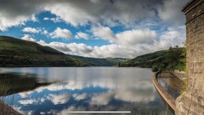 A tranquil lake with a stone building on the right, surrounded by hills and a partly cloudy sky. - Ty Fferm  Hen Coity Bach Farm, over looking Toal y fory (Talybont-on-Usk)