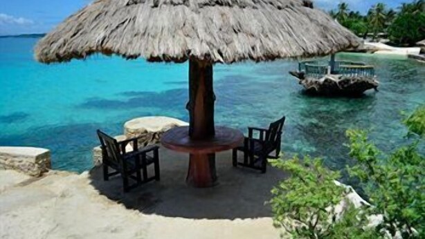 A thatched umbrella table with chairs, overlooking a clear blue sea with a boat in the distance. - Mangodlong Rock Resort (San Francisco)