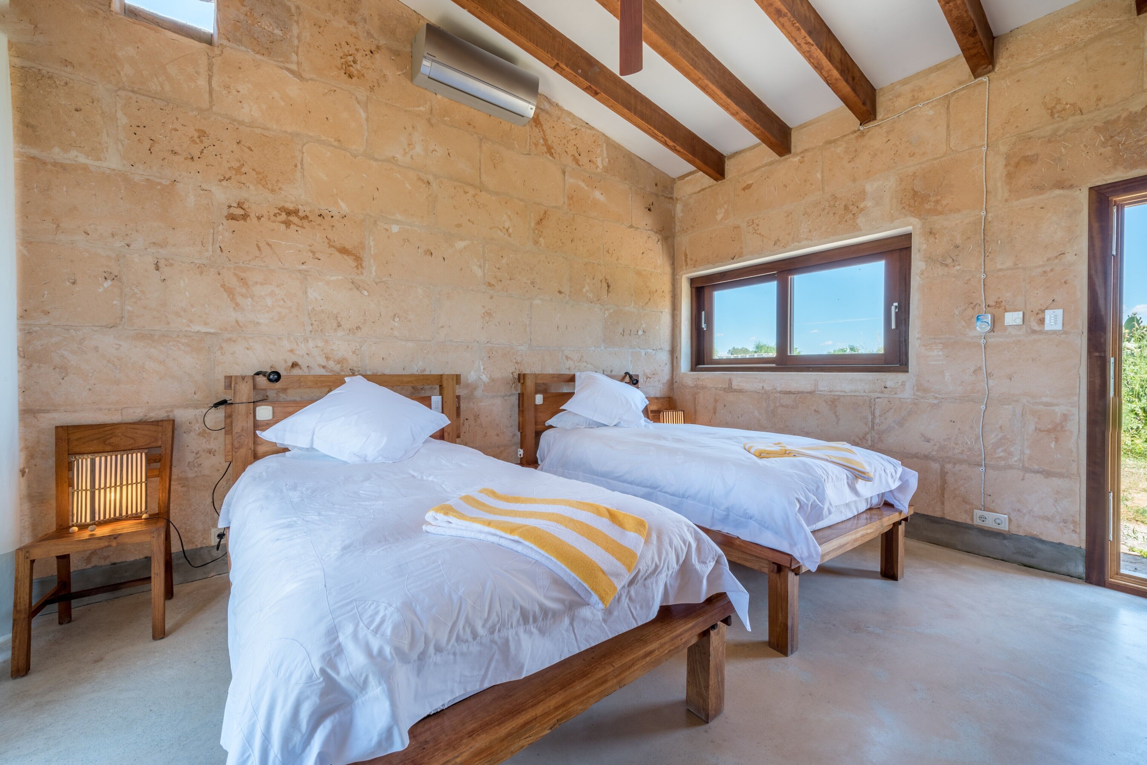 A room with two wooden beds, a window, and a stone wall.