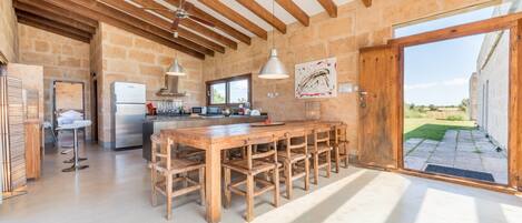 A spacious kitchen with a long wooden table, a built-in refrigerator, and a stone wall.