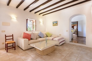 A living room with a sofa, a glass coffee table, a wooden chair, and a fireplace. - Beautiful Villa Can Cosmi with Wi-Fi, Pool, Terraces, Garden & Balcony; Parking Available (Es Canar)