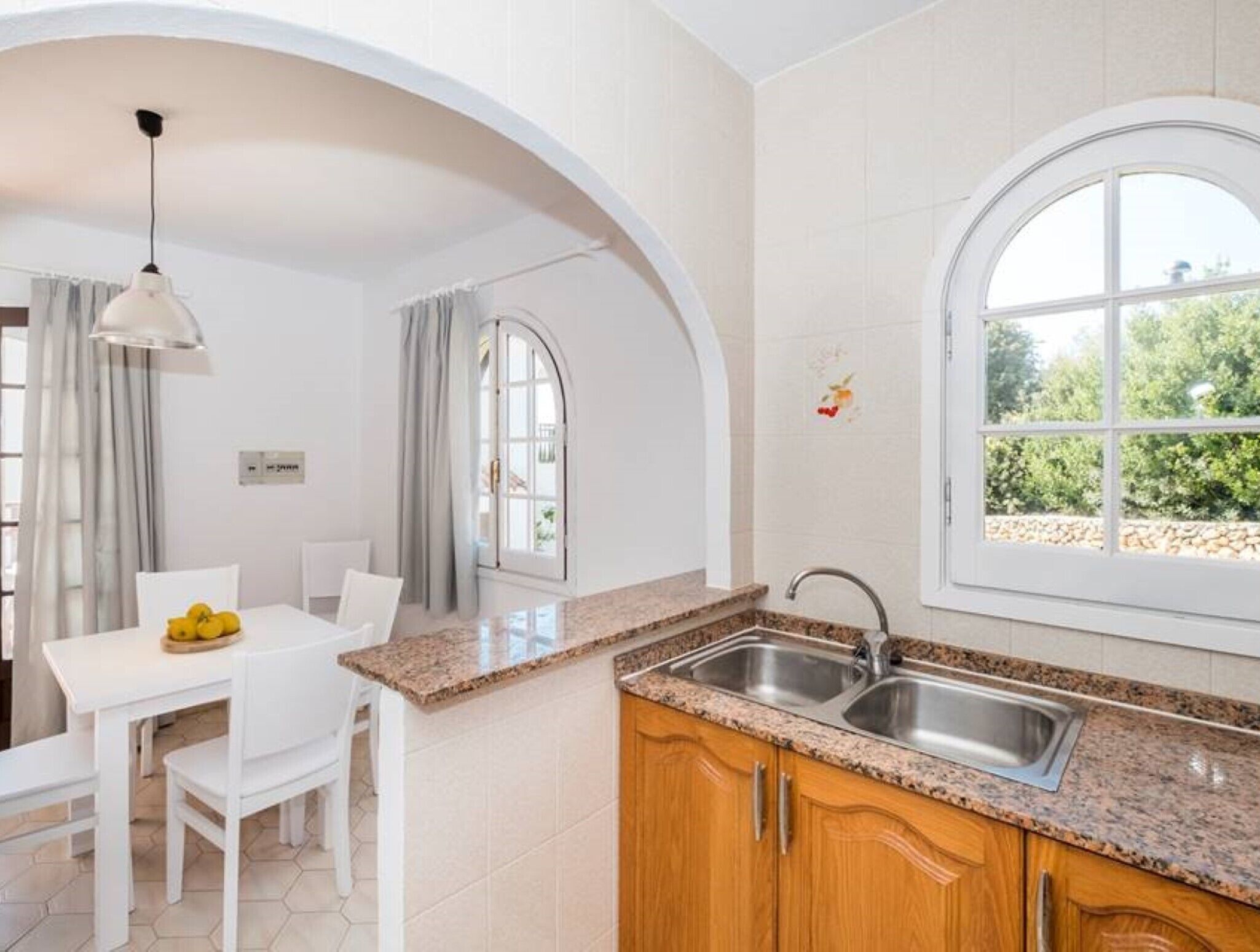 Eine moderne Küche mit Granitabdeckungen, Holzschränken, einer doppelten Spüle und einem Essbereich mit Tisch und Stühlen.