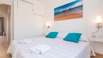 Ein Hotelzimmer mit einem Bett, zwei Kissen, einem Strandbild und einer Tür.