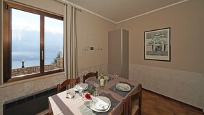 Ein Esszimmer mit Tisch für vier Personen, Meerblick durch ein großes Fenster und ein gerahmtes Bild an der Wand.