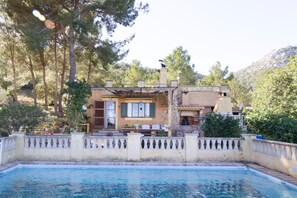 A house with a swimming pool, a patio with outdoor furniture, and a view of the surrounding trees and hills.