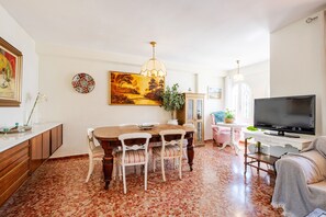Un comedor con una mesa y sillas de madera, un televisor y un cuadro grande en la pared.