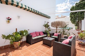 Un patio con mobiliario de mimbre, plantas en macetas y una pared blanca.