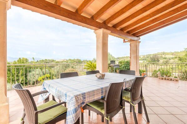 An outdoor patio with a table and chairs, a view of the countryside, and a pergola structure.