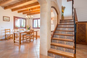 Un coin repas avec une table et des chaises en bois, un escalier orné de carreaux décoratifs et une vue à travers une arche.