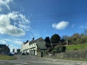 Vista de una calle con un edificio que muestra la inscripción 'The New Inn', destacando un estilo arquitectónico tradicional, un muro de piedra y un cielo azul despejado.