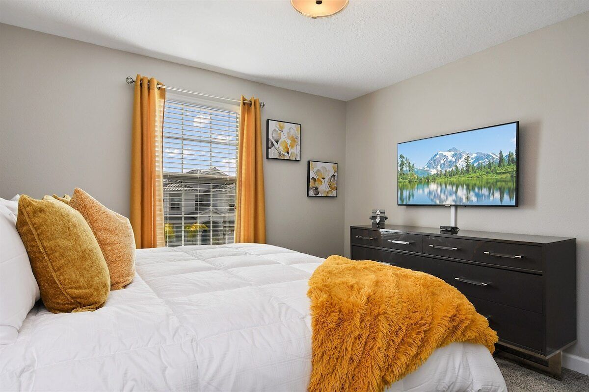 A bedroom with a bed, a dresser, and a television on the wall.