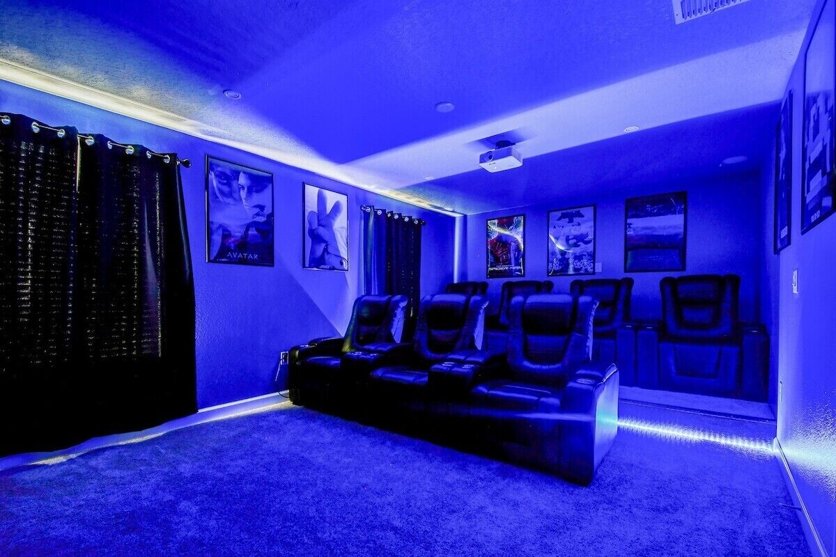 A home theater room with a blue hue, featuring a large screen, multiple seating areas, and wall-mounted posters.