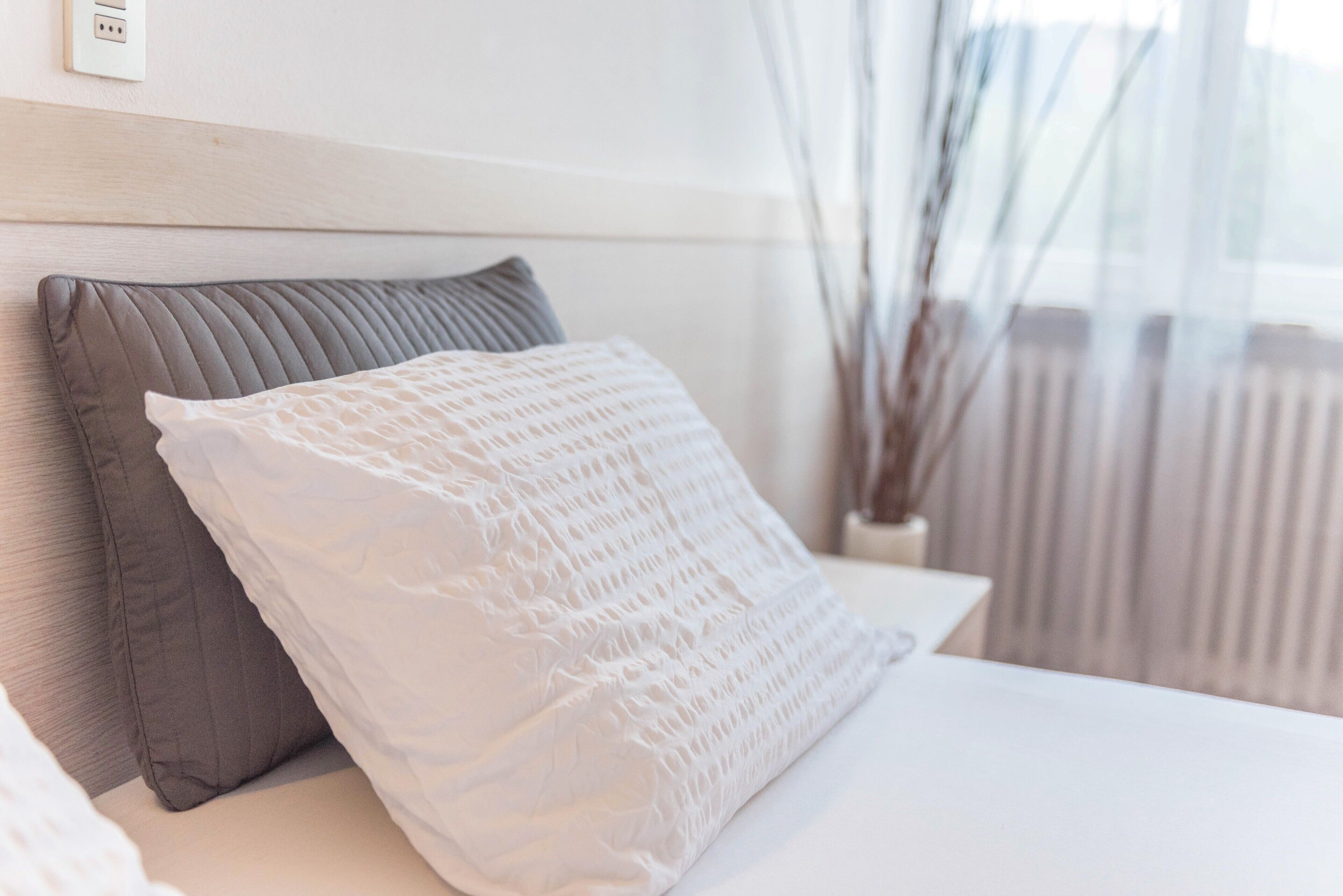 Ein Bett mit grau-weiß gestreifter Bettdecke, einem Holzkopfstück und einem Fenster mit Blick auf ein Gebäude.