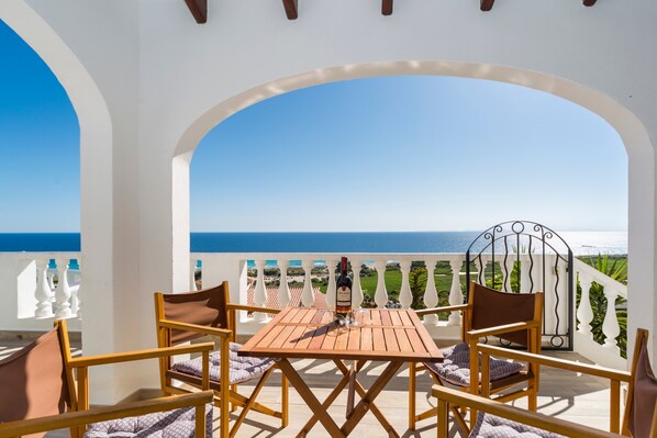 A terrace with a table and chairs, a bottle of wine, and a view of the sea. - Stunning sea view and pool – Villa Amoura (San Jaime Mediterráneo)