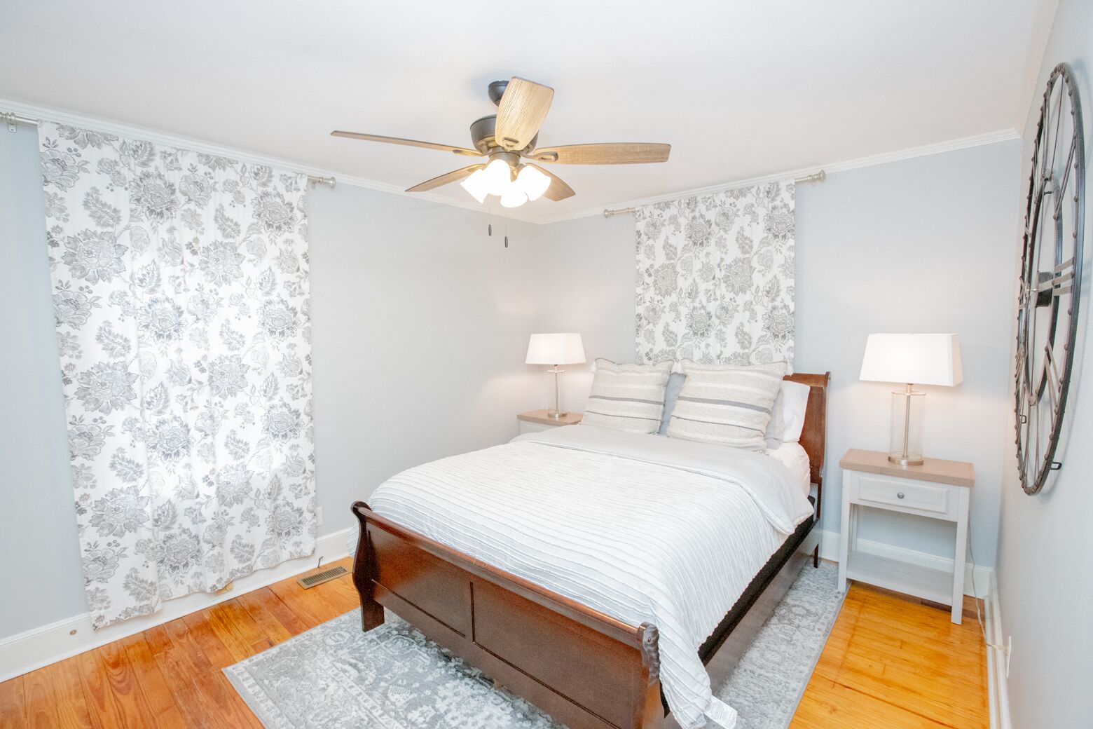 A bedroom with a wooden bed, two bedside tables with lamps, a ceiling fan, and patterned wallpaper.