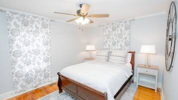 A bedroom with a wooden bed, two bedside tables with lamps, a ceiling fan, and patterned wallpaper.