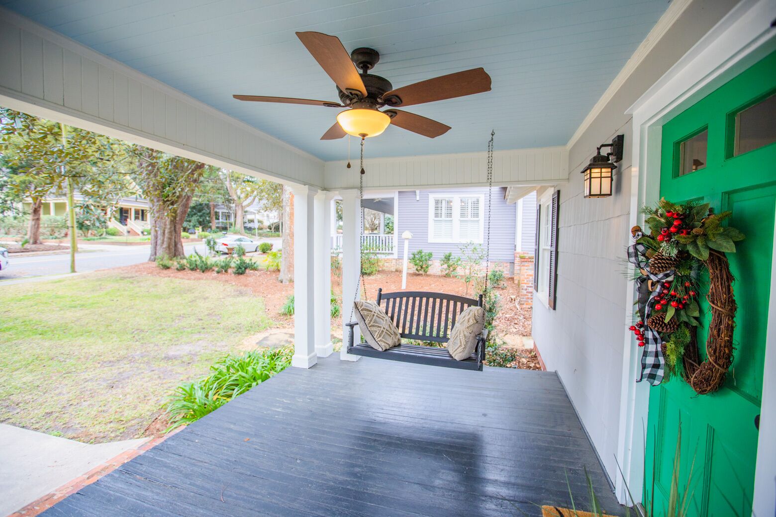 A porch with a ceiling fan, a bench, and a green door with a wreath.