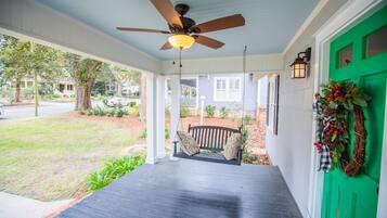 A porch with a ceiling fan, a bench, and a green door with a wreath.