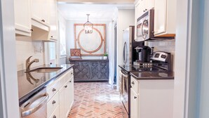 A modern kitchen with white cabinetry, a herringbone-patterned floor, and stainless steel appliances. - QUAIL COTTAGE - Downtown Thomasville! (Thomasville)