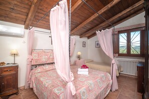 A bedroom with a four-poster bed, a wooden ceiling, a window with a view, and a radiator.