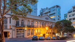 Un edificio histórico con arquitectura clásica, un estacionamiento y modernos rascacielos al fondo.
