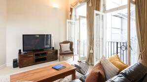 Una sala de estar con televisor, mueble de entretenimiento de madera, un sofá y una mesa de centro.
