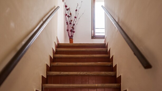 Una escalera con escalones de madera y barandillas de metal, que lleva a un ventanal con luz natural.
