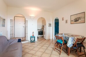 Un coin repas avec une table dressée pour quatre personnes, une cuisine en arrière-plan et un salon avec un canapé.