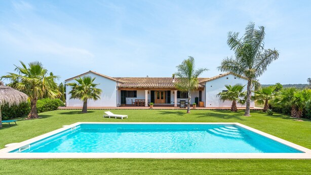 Ein Haus mit Schwimmbad, umgeben von Gras und Palmen.