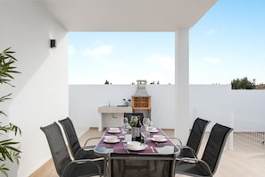 Una terraza en la azotea con una mesa de comedor para seis personas, rodeada de sillas, una parrilla y vistas de la ciudad.