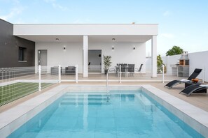 Una piscina con cerca blanca, sillas de descanso y un área de patio techada.