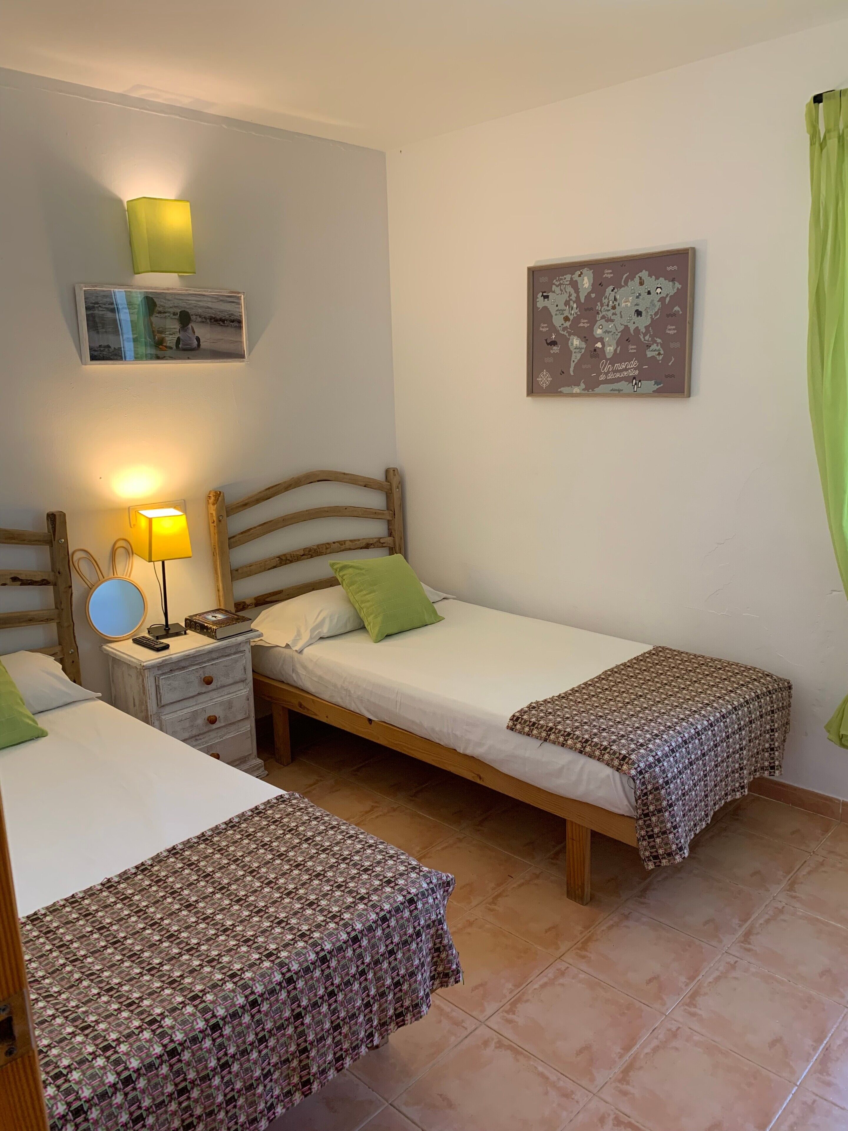 A room with two single beds, a nightstand with a lamp, a small table with a mirror, and a map on the wall.