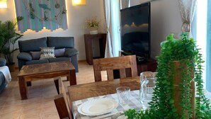 Una sala de estar con sofá, televisor, mesa de comedor con platos y vasos, y una obra de arte en la pared.