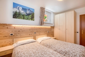 Une chambre avec deux lits, une tête de lit en bois, une fenêtre avec des rideaux et une armoire.