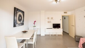 Moderni olohuone, jossa on ruokailutila, televisio ja ovi, joka johtaa toiseen huoneeseen.