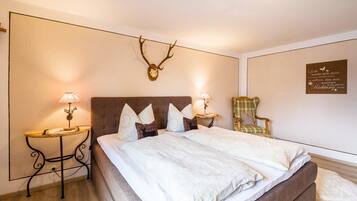 Une chambre à coucher avec un grand lit, deux tables de chevet avec des lampes, une chaise et une décoration murale représentant un crâne de cerf.