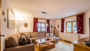 Un salon confortable avec un canapé, une table basse, un radiateur et une fenêtre ornée de rideaux rouges.