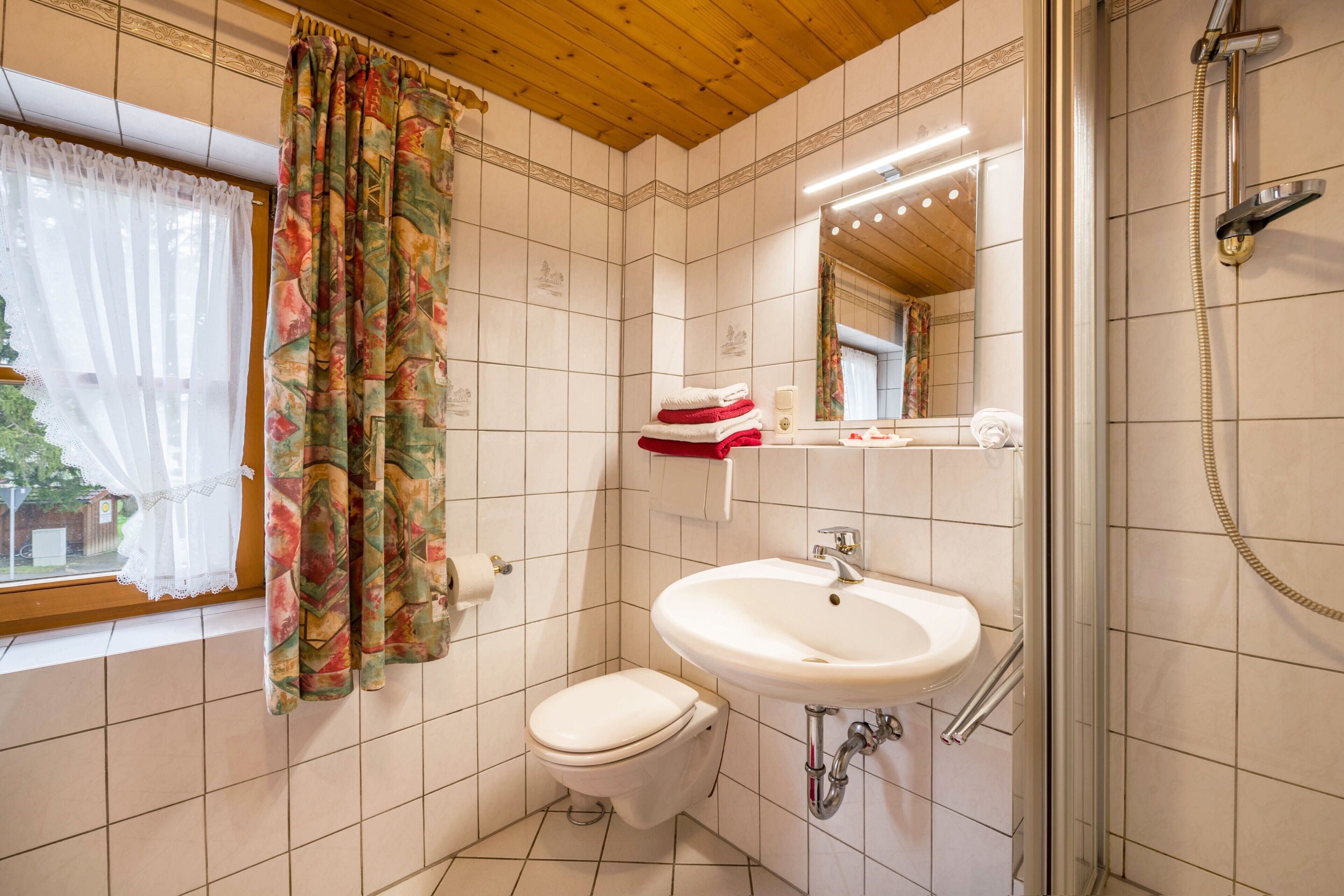 A bathroom with a toilet, sink, shower, and a window with curtains.