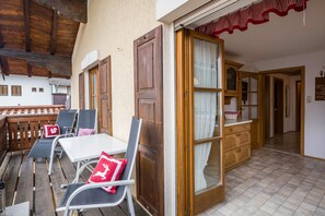 A room with a wooden ceiling, a white table with two chairs, a wooden door, and a glass door leading to a kitchen area. - Rustic Holiday Home Annelies with Wi-Fi, Garden, Terrace (Übersee)