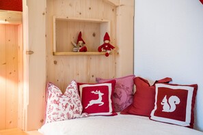 A bedroom with a wooden headboard, a shelf with two red gnome figures, and a bed with red and white pillows. - Rustic Holiday Home Annelies with Wi-Fi, Garden, Terrace (Übersee)