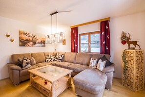 A cozy living room with a sectional sofa, a glass-top coffee table, and a decorative wall piece. - Rustic Holiday Home Annelies with Wi-Fi, Garden, Terrace (Übersee)