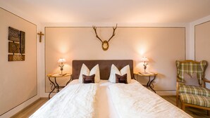 Une chambre à coucher avec un grand lit, deux tables de chevet avec des lampes, une croix accrochée au mur et une tête de cerf fixée au-dessus du lit.