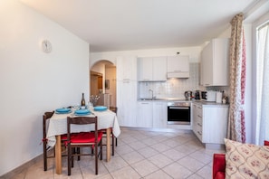 Une cuisine de taille réduite avec des meubles blancs, une table à manger avec des assiettes bleues et une chaise rouge.