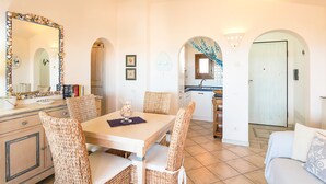 A dining area with wicker chairs, a table, and a mirror with a shell frame.