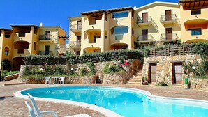A swimming pool with lounge chairs, a stone wall, and multi-story buildings with balconies.