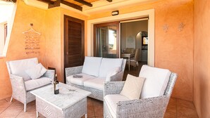 A covered outdoor seating area with wicker furniture, a wine bottle, and a hanging coat rack.