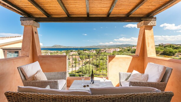 A balcony with wicker furniture, a table, and a bottle of wine.