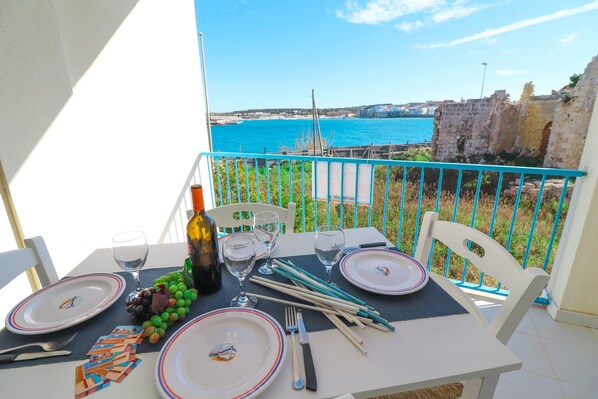 Une table dressée pour deux personnes, avec assiettes, couverts et une bouteille, offrant une vue sur la côte.